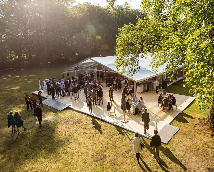 Aluhal tent voor een evenement op een open veld tussen de bomen.