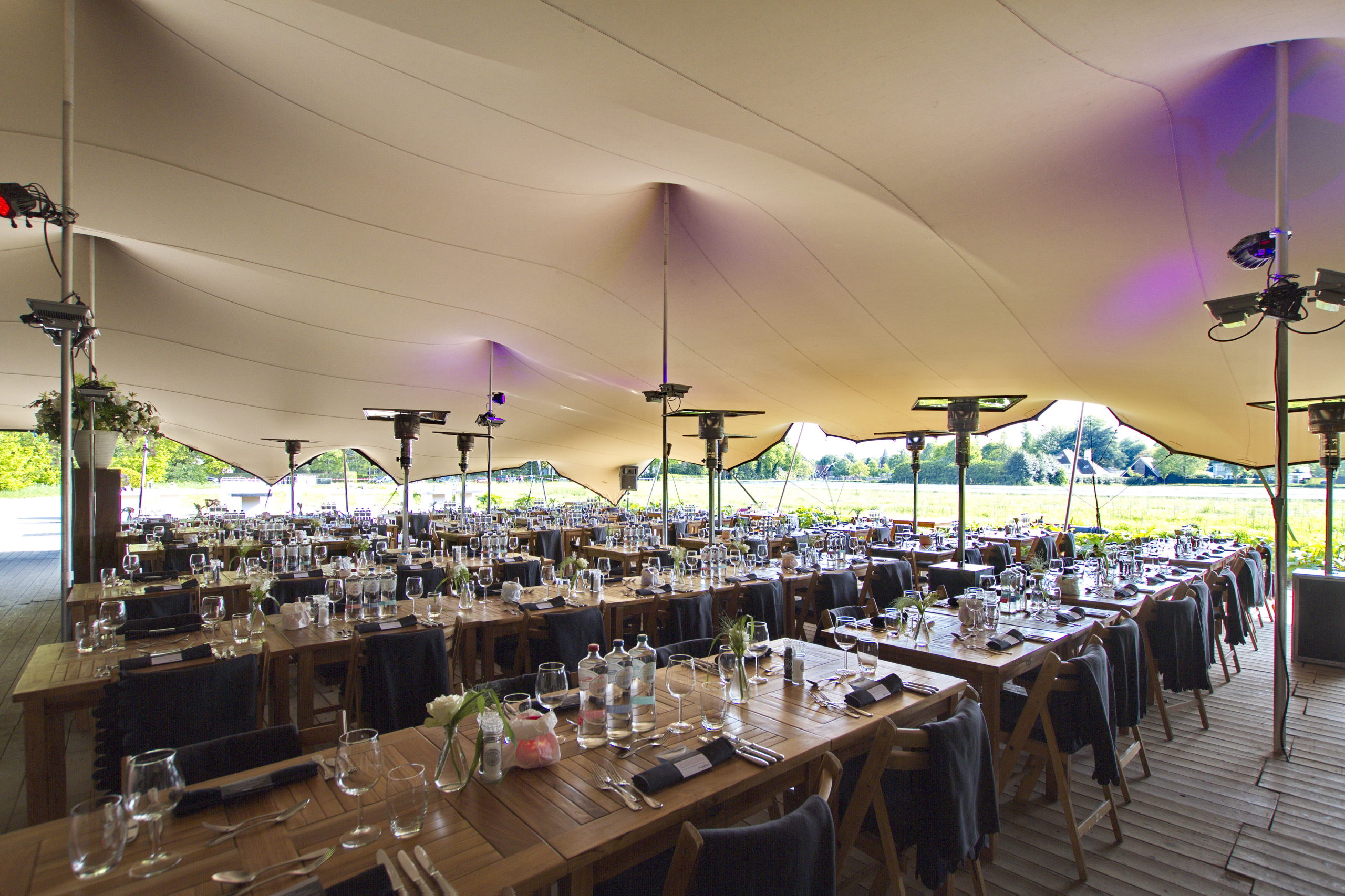 Terrasoverkapping met lange gedekte tafels onder de overkapping.