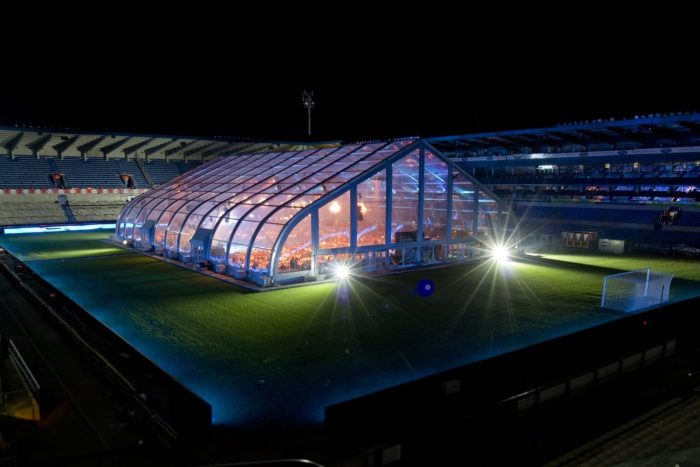 Transparante TFS tent op een voetbalveld in de avond.